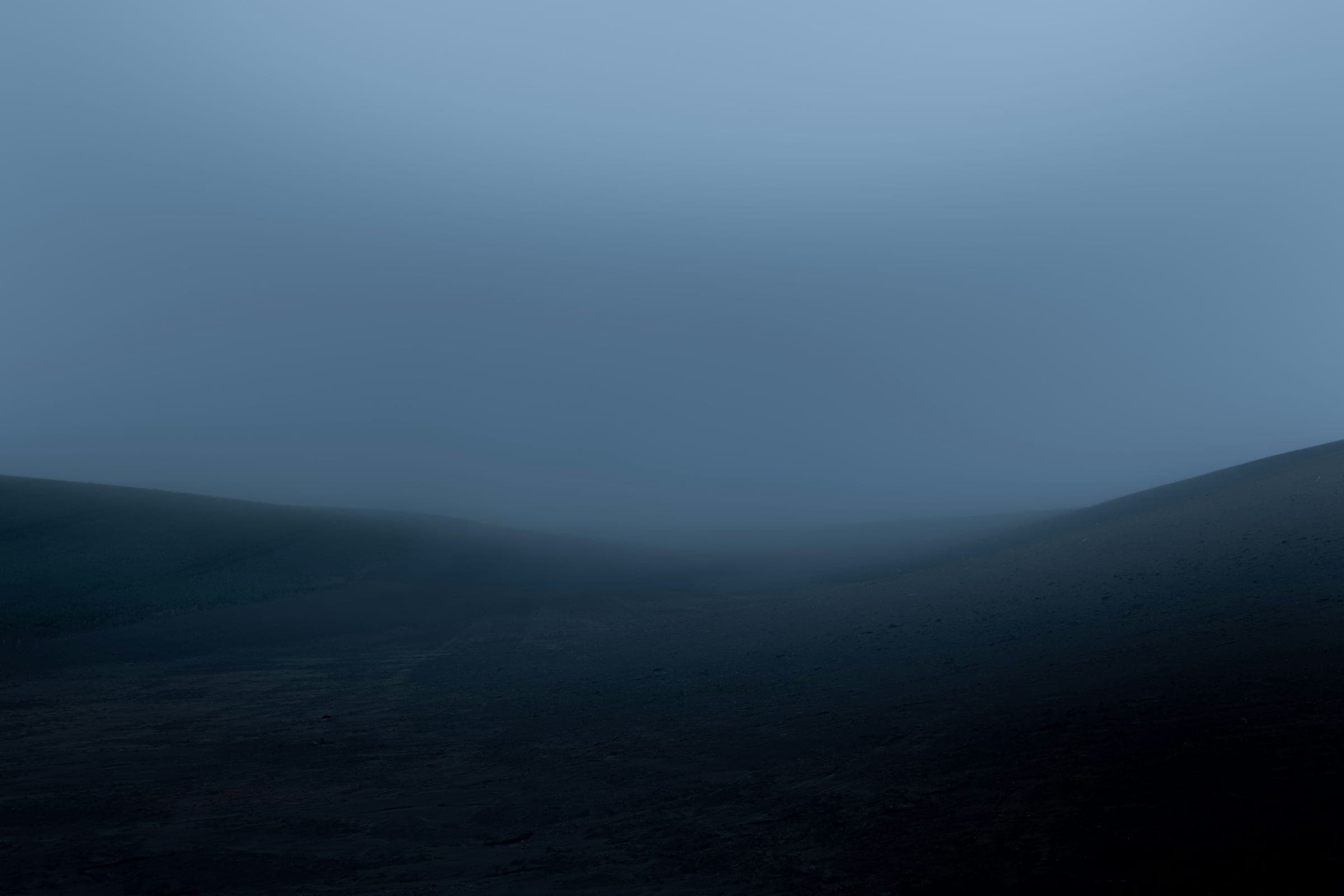 Empty, featureless hills fading into dense blue fog