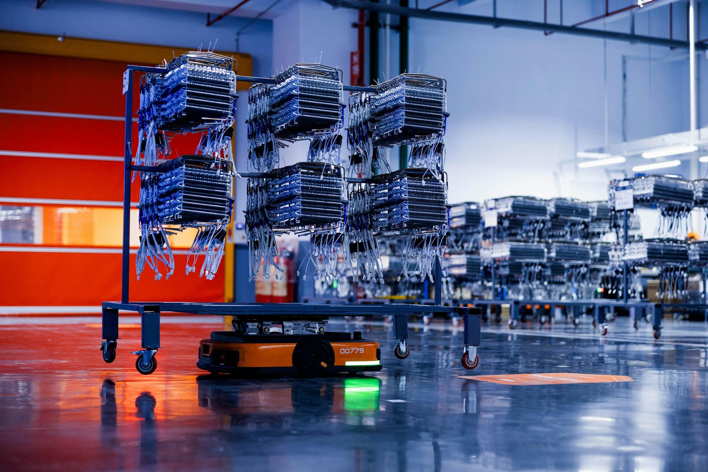 Autonomous mobile robot carrying a rack of components across a reflective factory floor