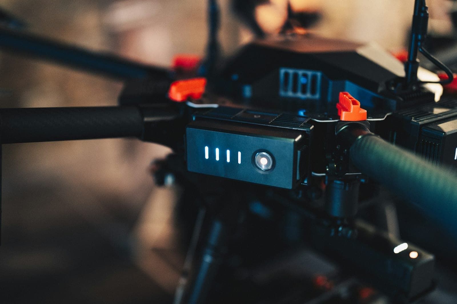 Close-up of a heavy-lift drone hub: battery charge LEDs, power button, carbon-fiber arms and orange arm locks