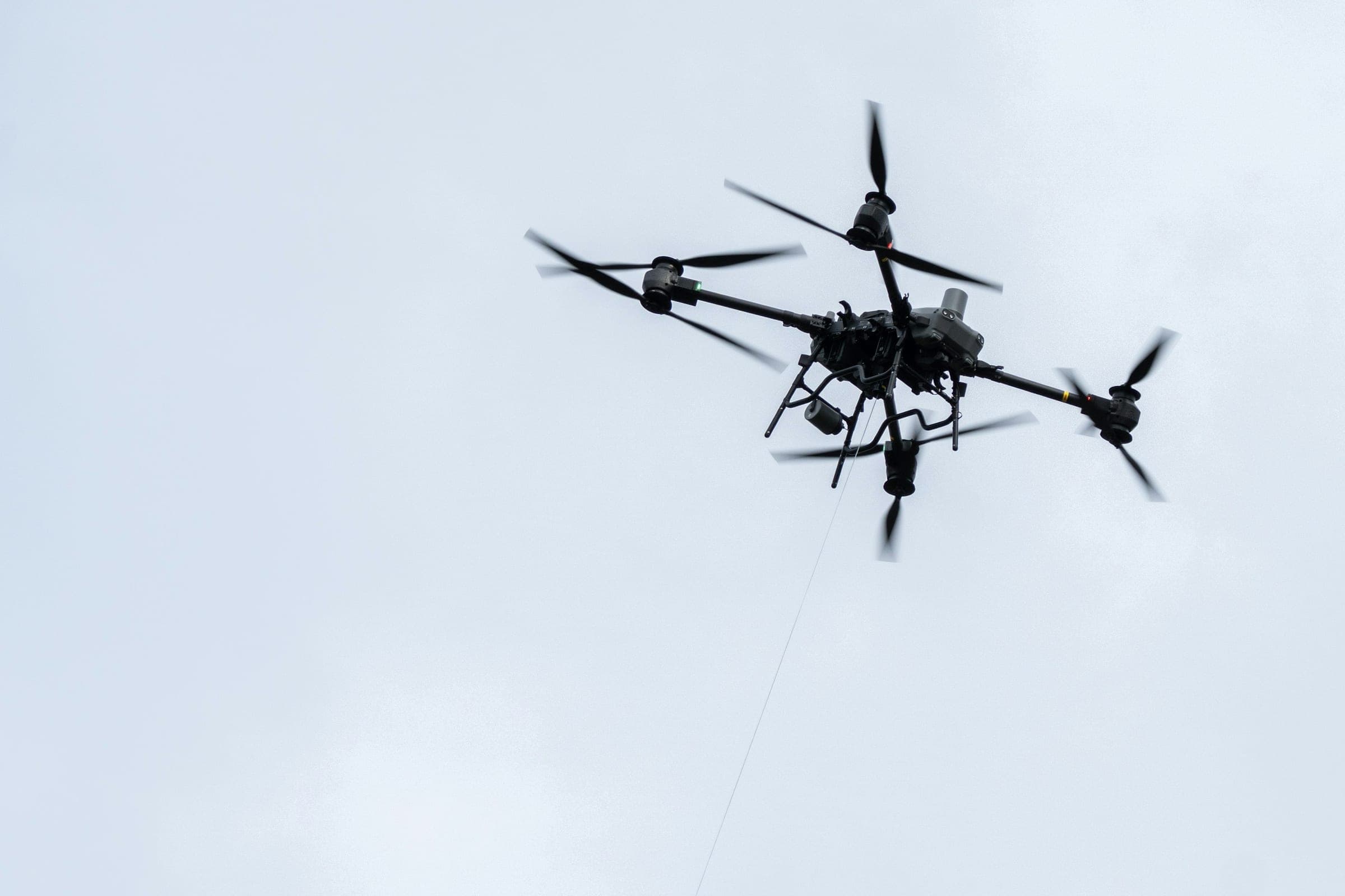 Industrial quadcopter with a sensor payload hovering against a pale overcast sky