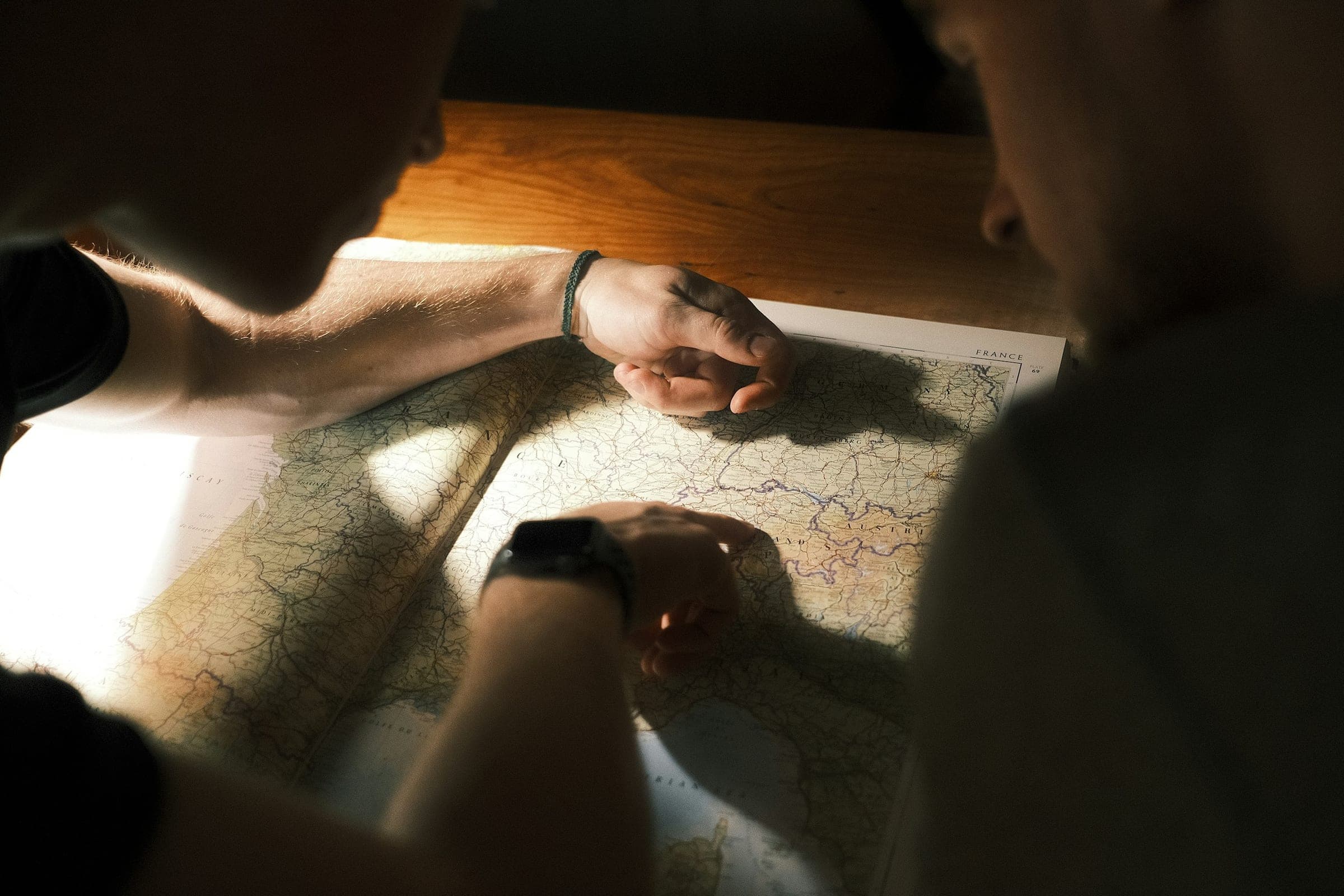 Two people leaning over a large paper map of Western Europe on a table in low, warm light