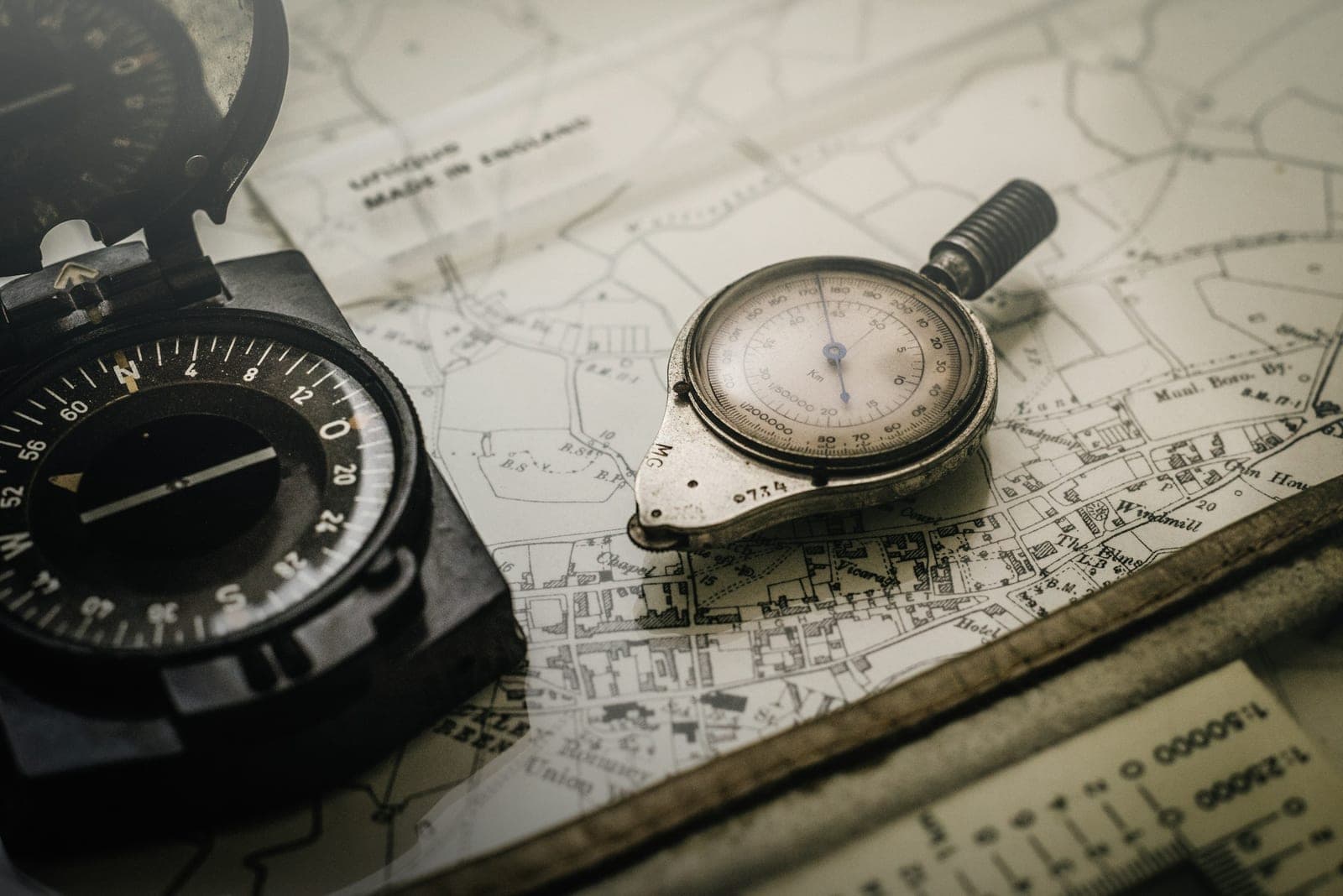 Lensatic compass and map measurer resting on a monochrome survey map, muted low-key tones